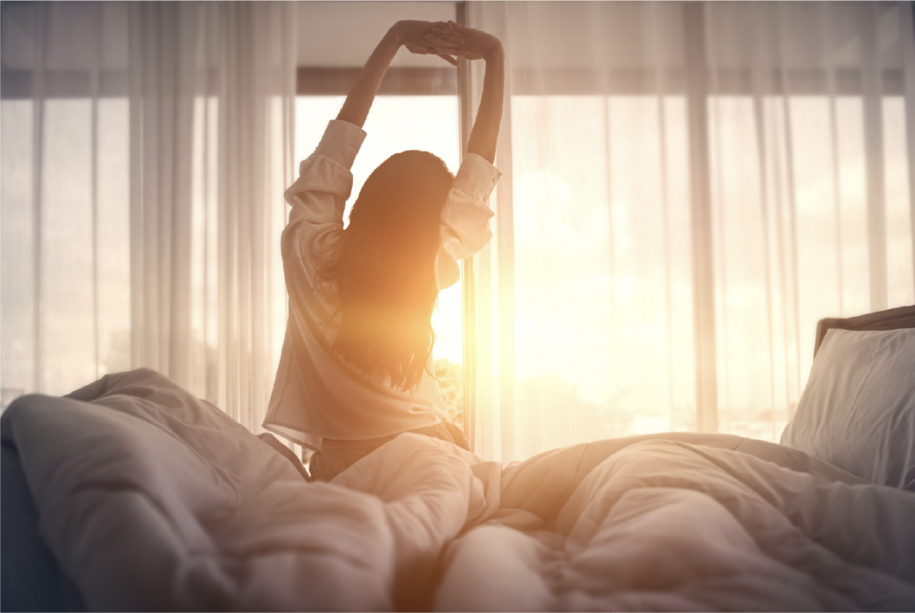 Woman waking up and stretching on her bed and watching the sunrise.
