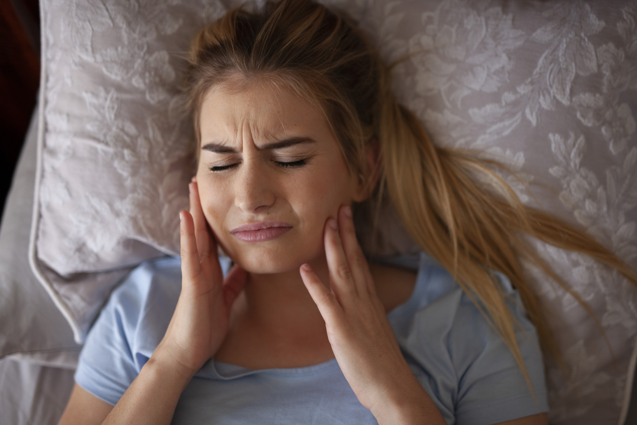 Woman in bed with TMJ pain holding her jaw.